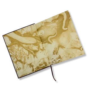 May include: Open journal with a brown cover and a gold and cream marbled design on the inside pages. A dark red ribbon bookmark extends from the spine. The journal is open, displaying the intricate patterns.