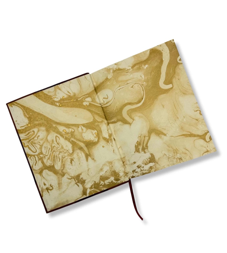 May include: Open journal with a brown cover and a gold and cream marbled design on the inside pages. A dark red ribbon bookmark extends from the spine. The journal is open, displaying the intricate patterns.