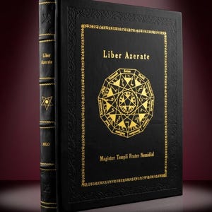 May include: A black book titled "Liber Azerate" with gold lettering and a gold geometric design. The book's spine has gold accents and the text "Liber Azerate" and "MLO". The book is on a reflective surface.