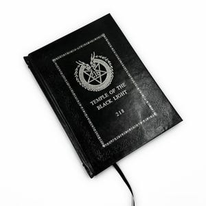K&ouml;nnte beinhalten: Schwarzes Buch mit gepr&auml;gtem Einband und silbernem Text. Das Cover zeigt einen dekorativen Rand, ein Pentagramm und den Text "TEMPLE OF THE BLACK LIGHT" und "218". Ein schwarzes Leseband ist angebracht.
