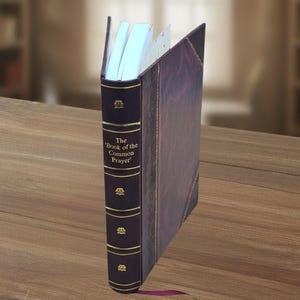 May include: A leather-bound book titled 'The Book of the Common Prayer' with gold accents. The book is dark purple with a matching spine and a purple ribbon bookmark. The pages are white and the book is open.