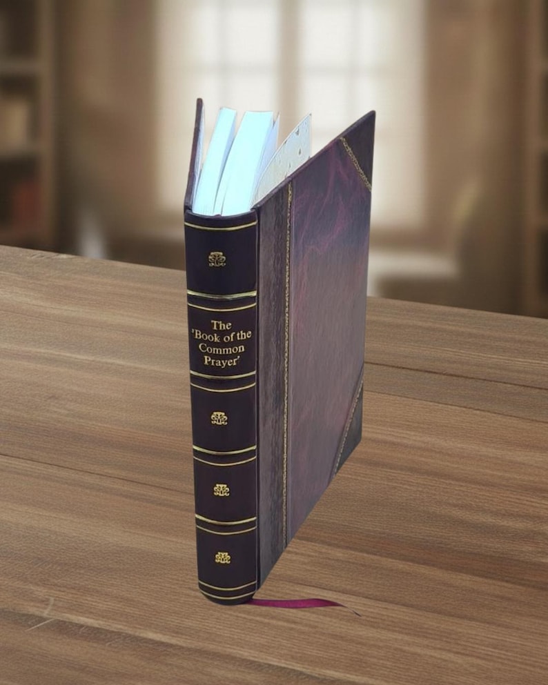 May include: A leather-bound book titled 'The Book of the Common Prayer' with gold accents. The book is dark purple with a matching spine and a purple ribbon bookmark. The pages are white and the book is open.
