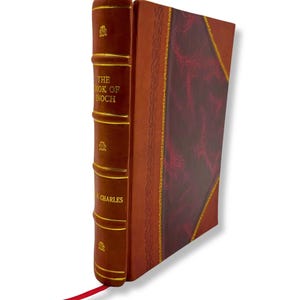 以下が含まれることがあります： 「THE BOOK OF ENOCH」というタイトルのハードカバー本。茶色の革の背表紙と表紙。背表紙には金色の文字と装飾的なアクセントがあります。本の表紙は、金色のトリムと赤いリボンブックマークが付いた、バーガンディのパターンが特徴です。