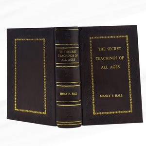 May include: A hardcover book titled "The Secret Teachings of All Ages" by Manly P. Hall. The book has a dark brown cover with gold lettering and decorative gold trim. The spine is also dark brown with gold text.