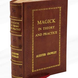 Peut inclure: Un livre &agrave; couverture rigide marron intitul&eacute; "Magick in Theory and Practice" par Aleister Crowley. La couverture pr&eacute;sente des lettres dor&eacute;es et des bordures d&eacute;coratives. Un signet en ruban rouge est visible.