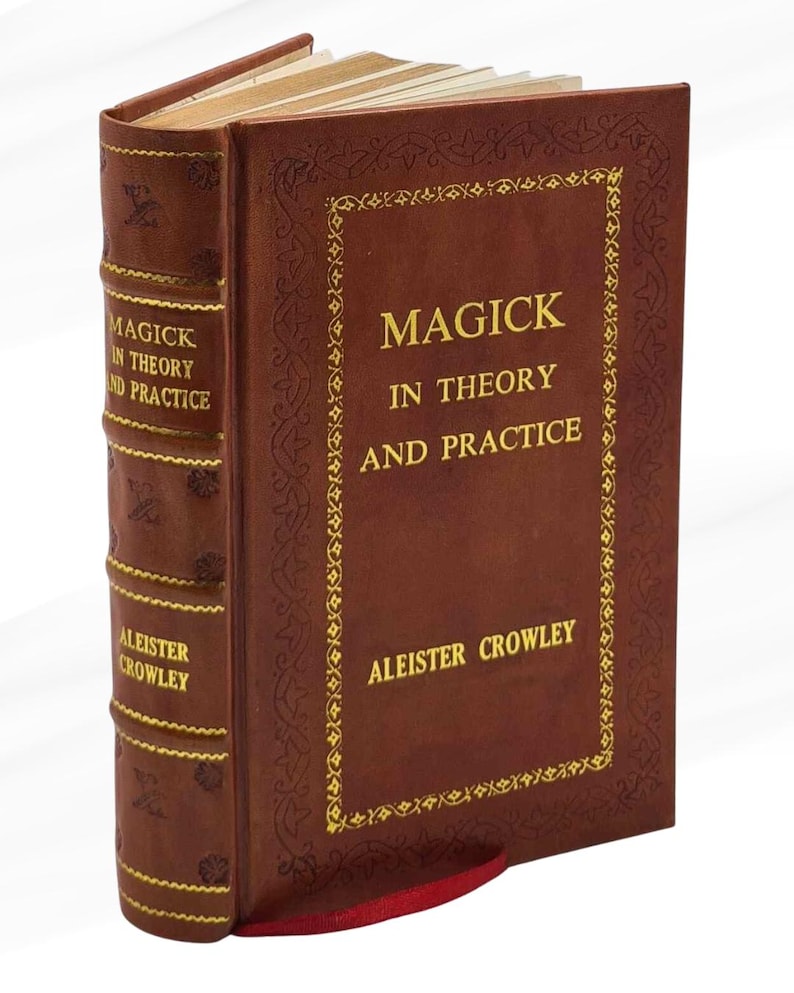 Peut inclure: Un livre &agrave; couverture rigide marron intitul&eacute; "Magick in Theory and Practice" par Aleister Crowley. La couverture pr&eacute;sente des lettres dor&eacute;es et des bordures d&eacute;coratives. Un signet en ruban rouge est visible.
