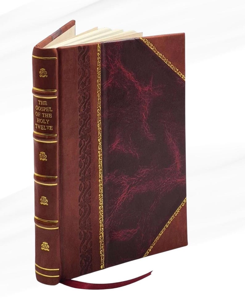 May include: A hardback book titled "The Gospel of the Holy Twelve." The book features a burgundy leather cover with gold detailing and a decorative spine. A burgundy ribbon bookmark is visible.