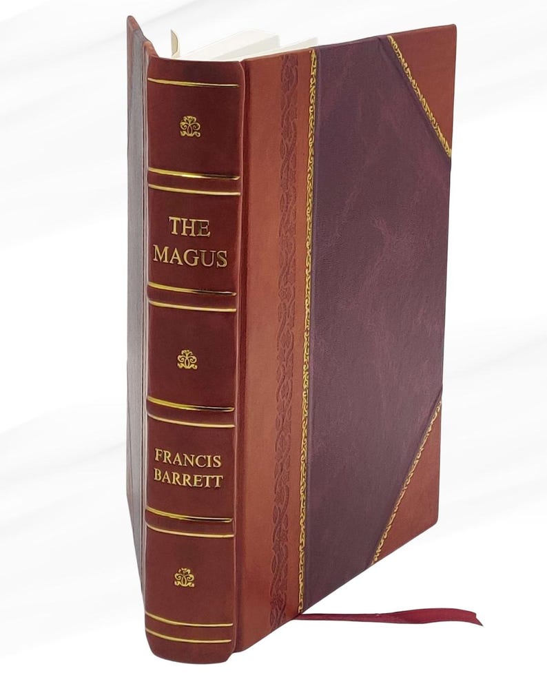 May include: A hardback book titled "The Magus" by Francis Barrett. The book features a burgundy spine with gold lettering and decorative details. The cover combines burgundy and brown leather with gold trim and a red ribbon bookmark.