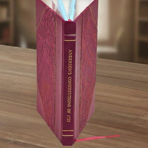 Peut inclure: Un livre relié en cuir bordeaux, intitulé "Anderson's Constitutions of 1723", est ouvert sur une surface en bois. Le dos du livre présente des lettres dorées, et un signet en ruban rouge dépasse des pages. Les pages du livre sont visibles.