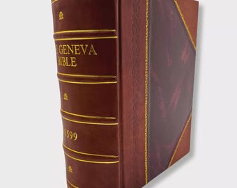 Puede incluir: Un libro encuadernado en cuero burdeos con letras y detalles dorados. El lomo muestra "GENEVA BIBLE" y el año "1599". La portada presenta un panel contrastante con un borde dorado.
