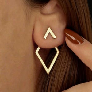 May include: Gold-colored geometric earrings. The earrings feature a small inverted V shape that sits on the earlobe, with a larger diamond shape hanging below. The design is modern and minimalist, suitable for everyday wear or special occasions.