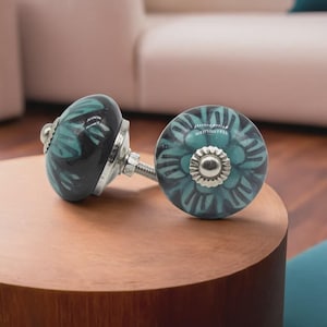 May include: Two decorative ceramic cabinet knobs. One knob is black with teal floral design, the other is teal with a silver center and a teal floral design. Both knobs have silver hardware.