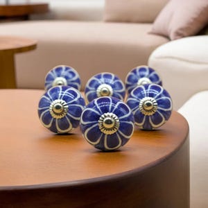 May include: Seven blue and white ceramic cabinet knobs with a floral design. Each knob has a silver-colored metal base. The knobs are arranged on a brown wooden surface.