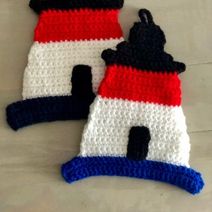 May include: Two crocheted lighthouse pot holders in red, white, and blue. The pot holders are shaped like lighthouses with black roofs and windows.