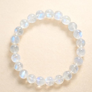 Op de afbeelding: Een ronde armband gemaakt van heldere, iriserende maansteen kralen. De kralen zijn bolvormig en aan elkaar geregen, waardoor een cirkelvorm ontstaat. De maansteenkralen hebben een subtiele, etherische gloed.