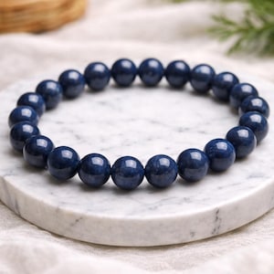 Könnte beinhalten: Ein kreisförmiges Stretch-Armband, bestehend aus glatten, runden, tiefblauen Perlen. Die Perlen haben eine polierte, reflektierende Oberfläche und sind zu einer durchgehenden Schlaufe aufgereiht, was ein einheitliches Erscheinungsbild erzeugt.