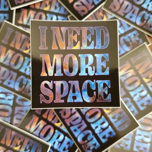 May include: A stack of stickers with a galaxy background and the text "I NEED MORE SPACE" in a retro font.