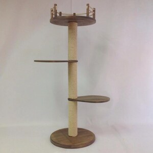 Könnte beinhalten: Ein Katzenbaum aus Holz mit mehreren Ebenen. Die Basis ist eine runde Plattform, die einen zentralen Pfosten aus Natur-Sisal-Seil trägt. Zwei ovale Plattformen und eine obere Plattform mit kleinem Zaun. Das Holz hat einen warmen Braunton.