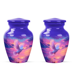 May include: Two blue urns with a glossy finish. Each urn features a serene scene of a white dove in flight against a sunset sky with pink, orange, and purple hues. The urns are designed for memorial purposes.