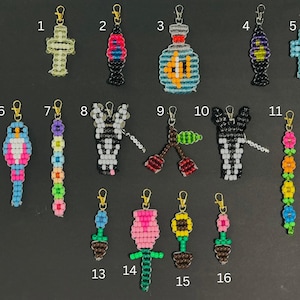 May include: Sixteen beaded charms with gold-tone lobster clasps, numbered 1 through 16. Designs include a cross, lava lamps, a fishbowl, a bird, flowers, cherries, a zebra head, and potted plants in various colors like pink, blue, and yellow.