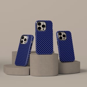 May include: Three navy blue phone cases with a white polka dot pattern are displayed on grey pedestals. The cases have a glossy finish and are designed to fit a smartphone. The cases are angled to show the design.