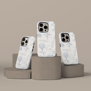 May include: Three white phone cases with a blue floral design and the text "Faith, Hope, Love, 1 Corinthians 13:13". The cases are displayed on grey geometric blocks.