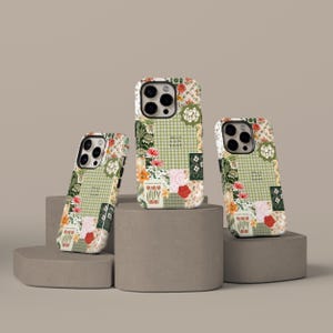 Pode incluir: Três capas de telemóvel com um design de patchwork floral. As capas apresentam uma mistura de xadrez verde, padrões florais e o texto "Good Vibes, Hello, Sunshine". As capas são exibidas em plataformas cilíndricas cinzentas.