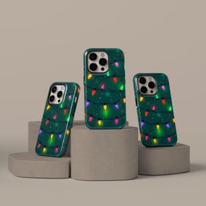 May include: Three green phone cases with a festive Christmas lights design. The cases feature colorful string lights against a dark green background. The cases are displayed on gray pedestals.