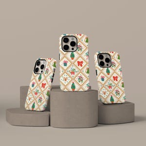 May include: Three phone cases with a festive Christmas pattern. The cases feature a repeating design of Christmas trees, bows, and gift boxes on a cream background with gold accents. The cases are displayed on gray pedestals.