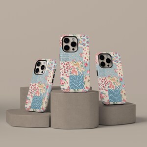 May include: Three phone cases with a patchwork design. The cases feature a mix of floral patterns, polka dots, and solid colors in pink, blue, and cream. The cases are displayed on gray concrete blocks.