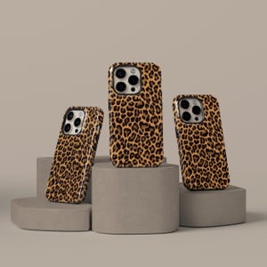 May include: Three phone cases with a leopard print design. The cases are in different positions, showcasing the design on the front and sides. The cases are brown and black, with a tan background.
