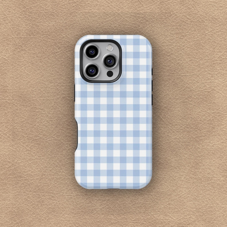 May include: A light blue and white gingham pattern phone case. The case has a camera cutout and button cutouts. The phone case is on a tan surface.