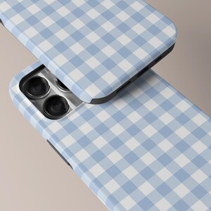 May include: Two phone cases with a light blue and white gingham pattern. The cases are shown at an angle, with the camera lenses visible on one. The cases have a black border and a glossy finish, creating a clean and modern look.