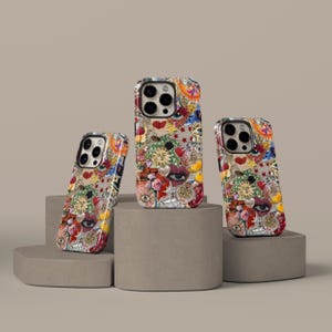 May include: Three phone cases with a vibrant collage design featuring hearts, eyes, suns, and flowers. The cases are displayed on grey geometric pedestals against a neutral backdrop. The cases have a glossy finish.