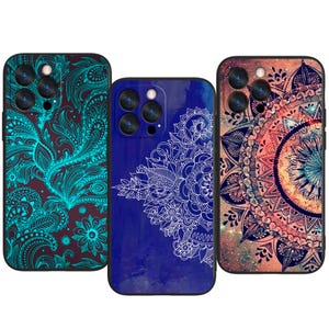 May include: Three phone cases with detailed patterns. One case has a teal floral design on a dark brown background. Another is a deep blue with a white floral design. The third case features a mandala design with orange and pink hues.