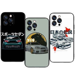 Könnte beinhalten: Drei Handyhüllen mit Auto-Designs. Eine schwarze Hülle zeigt eine türkisgrüne Sportlimousine mit japanischem Text. Eine graue Hülle hat eine Godzilla- und Autografik. Die weiße Hülle zeigt drei Autos mit japanischem Text und roten Akzenten.