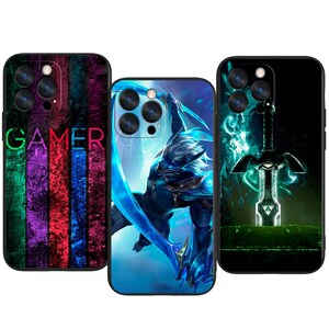 Puede incluir: Tres fundas para teléfono con diseños únicos. Una funda presenta la palabra "GAMER" en verde y rojo sobre un fondo a rayas colorido. Otra muestra un guerrero azul, y la tercera una espada brillante.