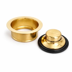 May include: A gold-toned metal sink drain flange with a matching gold-toned metal sink stopper. The stopper features a circular black rubber gasket around its base, designed to create a seal when inserted into the drain flange opening.