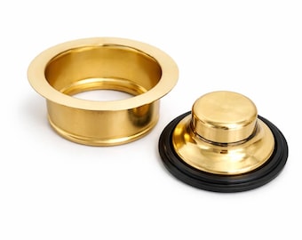 May include: A gold-toned metal sink drain flange with a matching gold-toned metal sink stopper. The stopper features a circular black rubber gasket around its base, designed to create a seal when inserted into the drain flange opening.