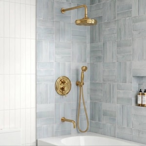 May include: A brushed gold shower system featuring a wall-mounted rainfall showerhead, a circular control valve with a lever handle, a handheld shower wand with a flexible hose, and a bath spout, all installed against light blue rectangular tiles.