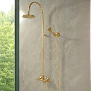 May include: A gold-colored shower fixture with a rain shower head and a handheld showerhead. The fixture has a curved arm and a control panel with cross-shaped handles. The showerhead is round and has multiple spray holes.