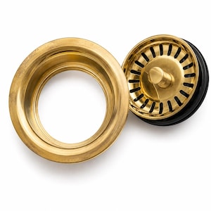 May include: A brass kitchen sink drain assembly consisting of a circular flange with a smooth metallic finish and a matching removable strainer basket featuring a central knob and a series of vertical slots, paired with a black rubber gasket seal.