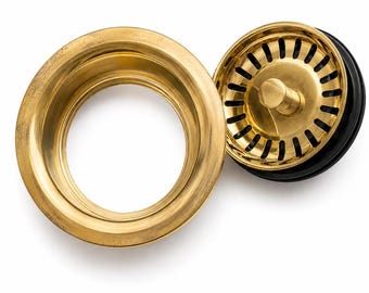 May include: A brass kitchen sink drain assembly consisting of a circular flange and a removable strainer basket. The strainer features a central knob and a series of vertical slots for water drainage, with a black rubber gasket visible underneath.