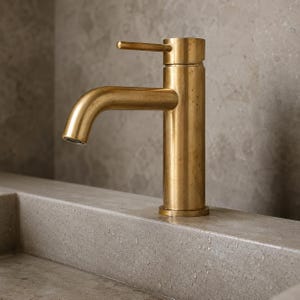 May include: A single-handle bathroom faucet with a brushed brass finish. The faucet features a cylindrical body and a curved spout with a lever handle positioned at the top. The metal surface has a matte, slightly weathered texture throughout.