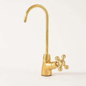 Puede incluir: Un grifo dorado con un caño curvo y un mango en forma de cruz. El grifo es de metal y tiene un acabado brillante. El diseño es simple y elegante, adecuado para una cocina o un baño.