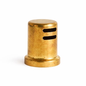 May include: A cylindrical brass object with a flared base and two horizontal slots near the top. The metallic surface has a slightly aged appearance, suggesting a vintage or industrial aesthetic. The object is isolated against a white background.