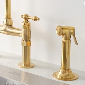 Puede incluir: Un grifo de cocina en oro cepillado con un rociador lateral. El grifo cuenta con un ca&ntilde;o de arco alto y una manija de palanca &uacute;nica. El rociador lateral es una unidad cil&iacute;ndrica a juego con una palanca, montados sobre un fregadero.