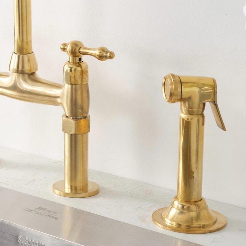 Puede incluir: Un grifo de cocina en oro cepillado con un rociador lateral. El grifo cuenta con un ca&ntilde;o de arco alto y una manija de palanca &uacute;nica. El rociador lateral es una unidad cil&iacute;ndrica a juego con una palanca, montados sobre un fregadero.
