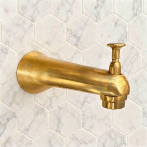 May include: A wall-mounted bathtub faucet spout finished in a brushed brass tone. The fixture features a cylindrical body that extends horizontally from the wall, topped with a small vertical diverter knob and a circular base plate.