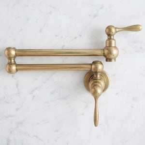 May include: A brass pot filler faucet with a swing arm design. The faucet has a curved spout and a lever handle. The finish is a warm, antique brass color. The faucet is mounted on a white marble wall.